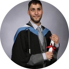 Abdul Eneser at his graduation, wearing a gown and holding his degree scroll.