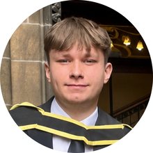 Luke Holmes at his graduation, wearing a gown and hood.